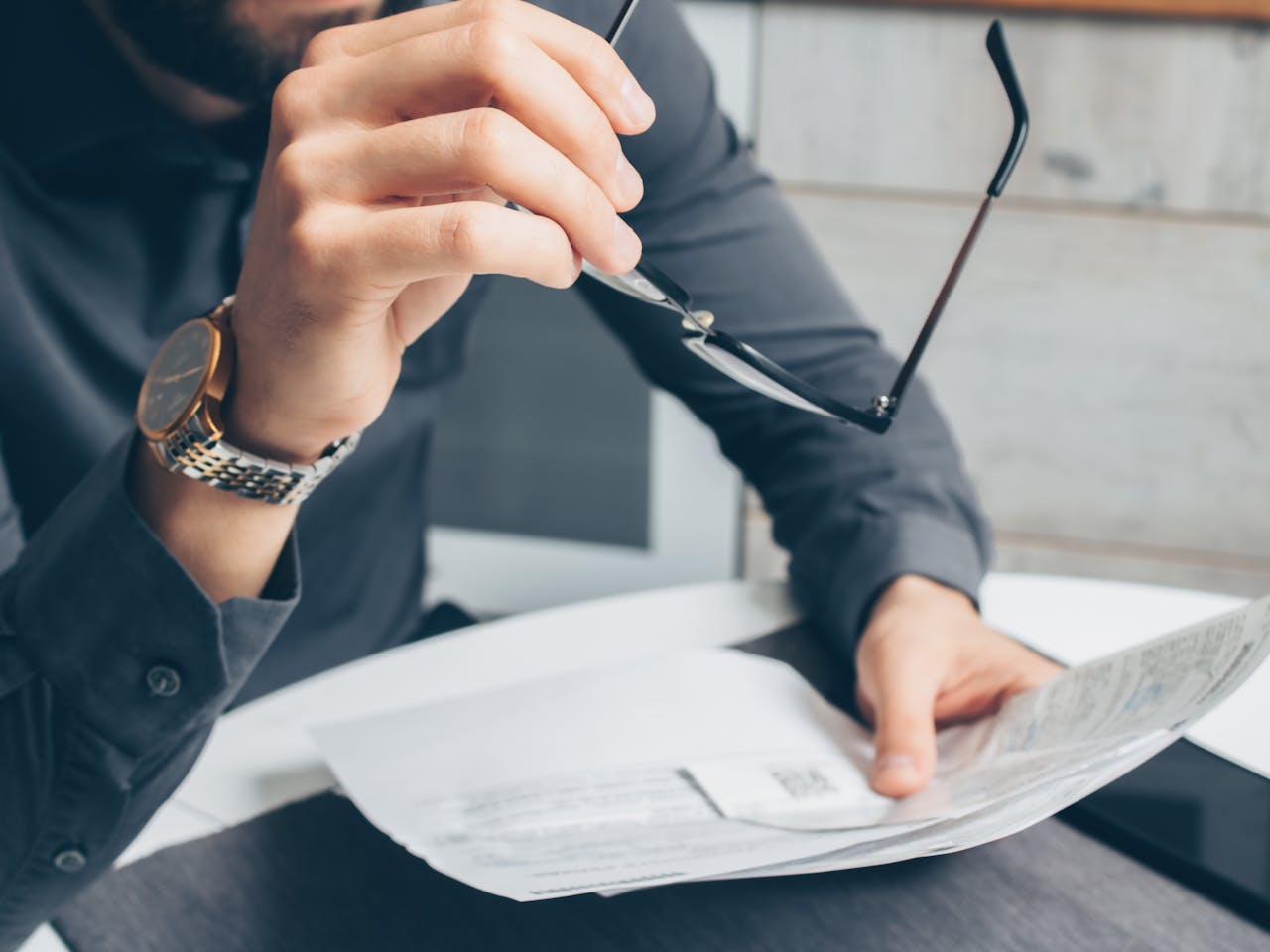 who-we-are Man in formal attire reviewing paperwork, holding glasses. Business setting.
